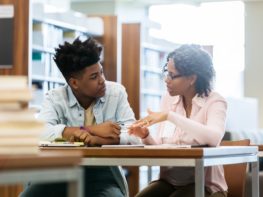 A teacher and a student of color, sitting and talking in a library