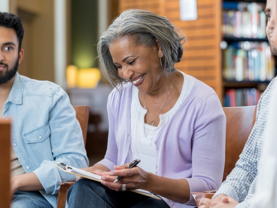 Older teacher of color, with a clipboard, in a group, laughing